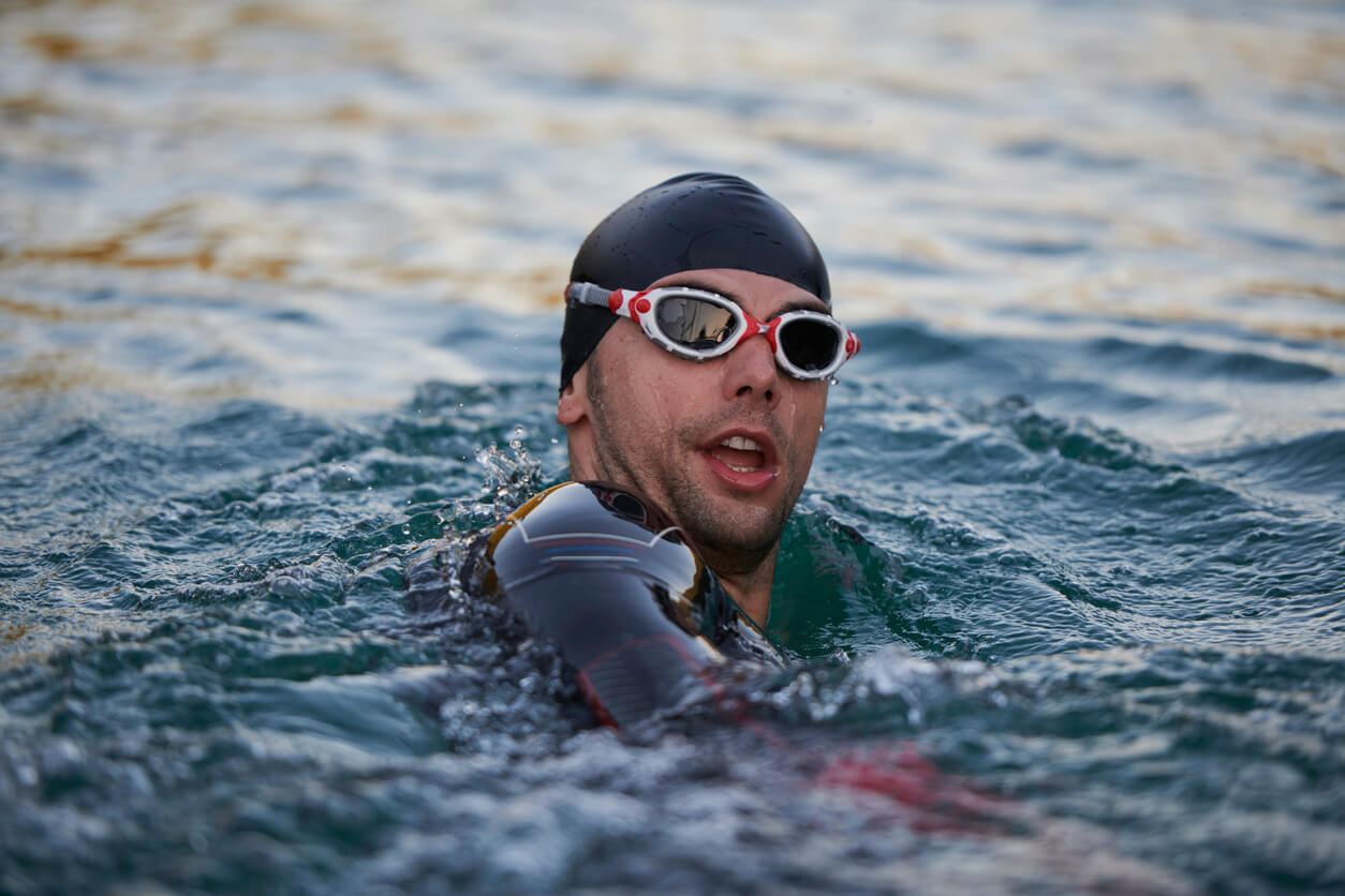 man wearing swim cap, goggles and wetsuit swimming in a lake