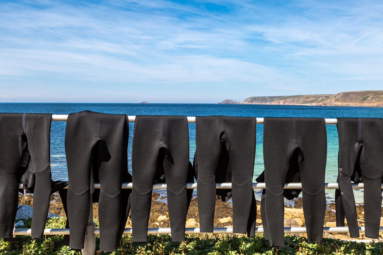 wetsuits hanging on a rail in front of a Cornwall beach scene