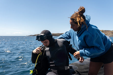 diving instructor helping a diver prepare their gear on the boat 
