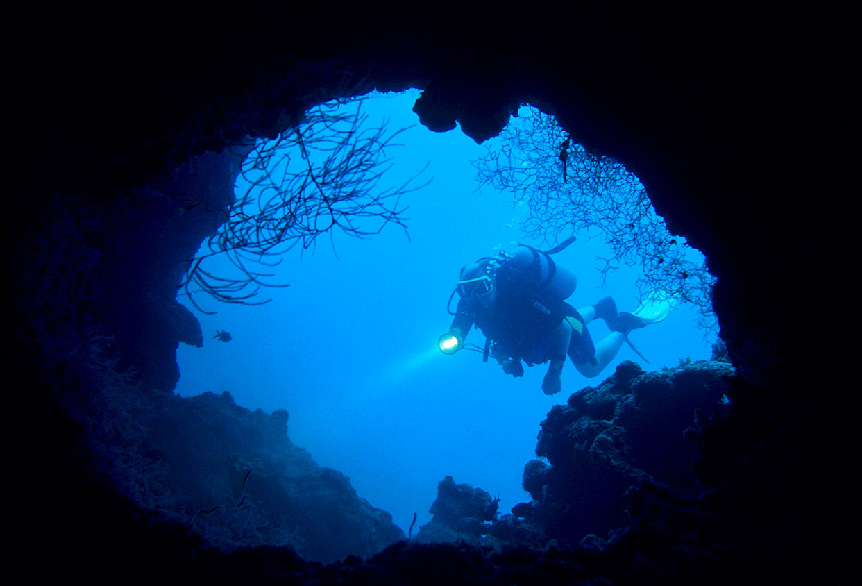 scuba diver swimming towards a cave with a torch